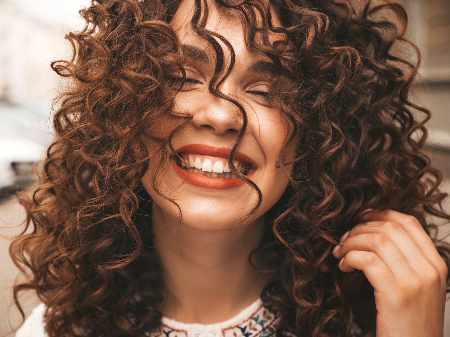 A woman with curly hair is smiling with her eyes closed.