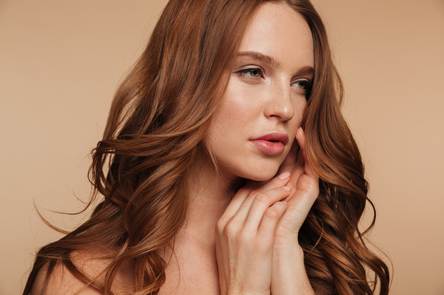Portrait of a beautiful young woman with long brown hair touching her face over beige background