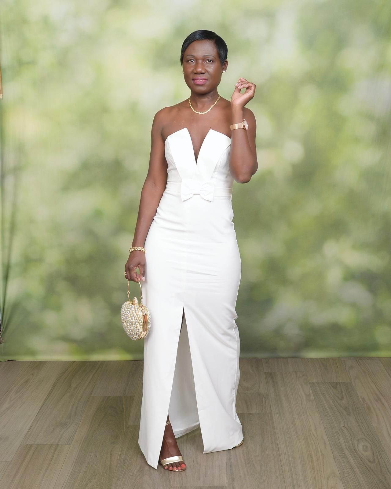 Woman in a white strapless gown posing with a clutch against a soft green backdrop