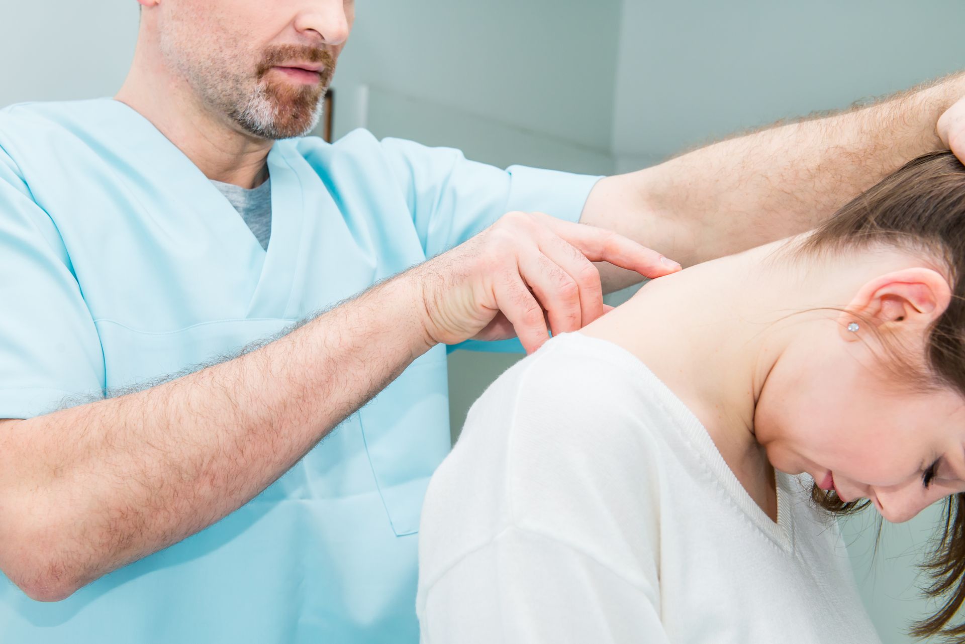 Chiropractor adjusting a woman's neck in a light-filled office. The woman bends, while the doctor presses.