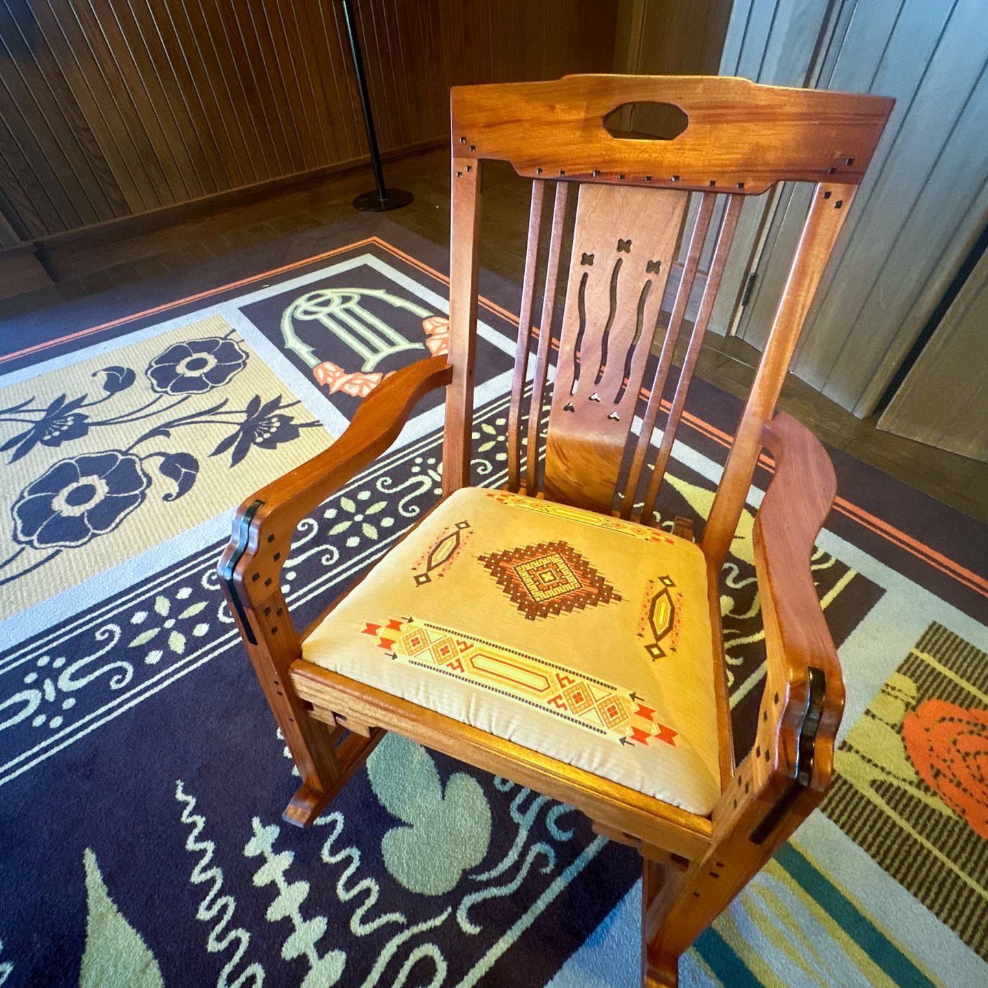 A wooden chair with a yellow cushion sits on a rug