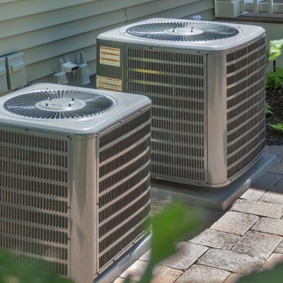Two air conditioners are sitting on the side of a house.