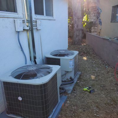 Two air conditioners are sitting on the side of a building.
