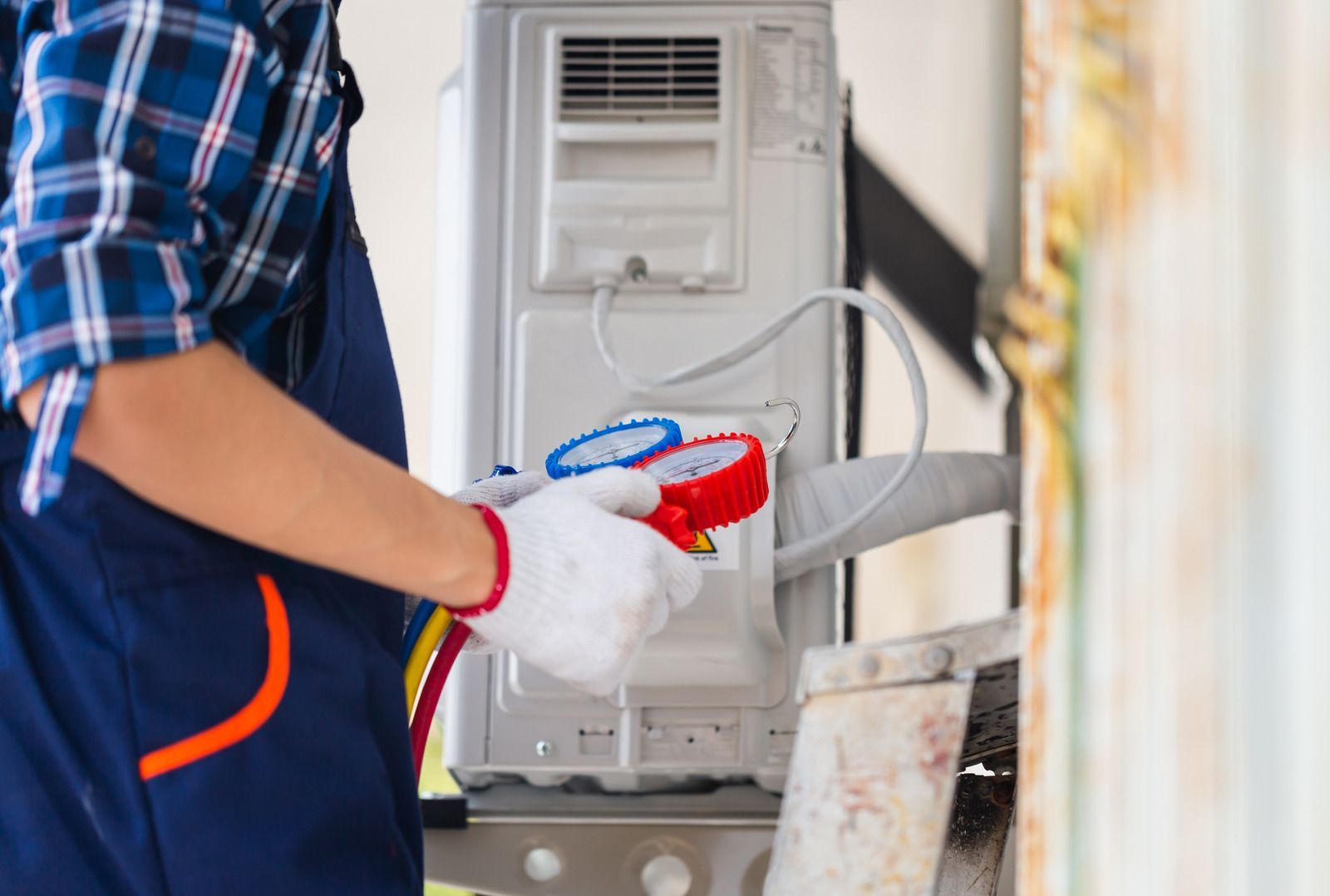 A man is working on an air conditioner with a gauge.