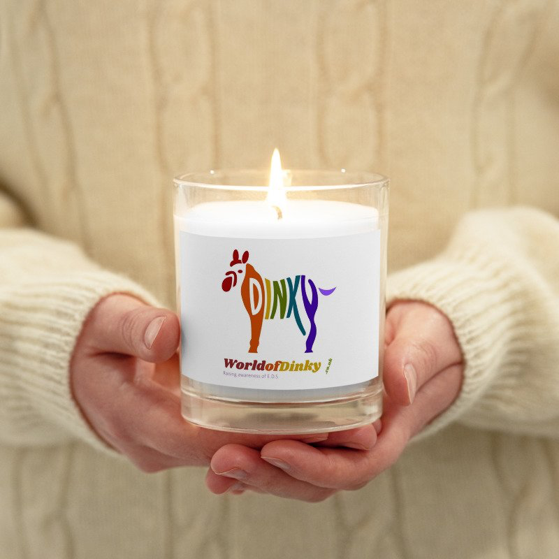 A pair of hands holding a glass jar candle with a lit flame.