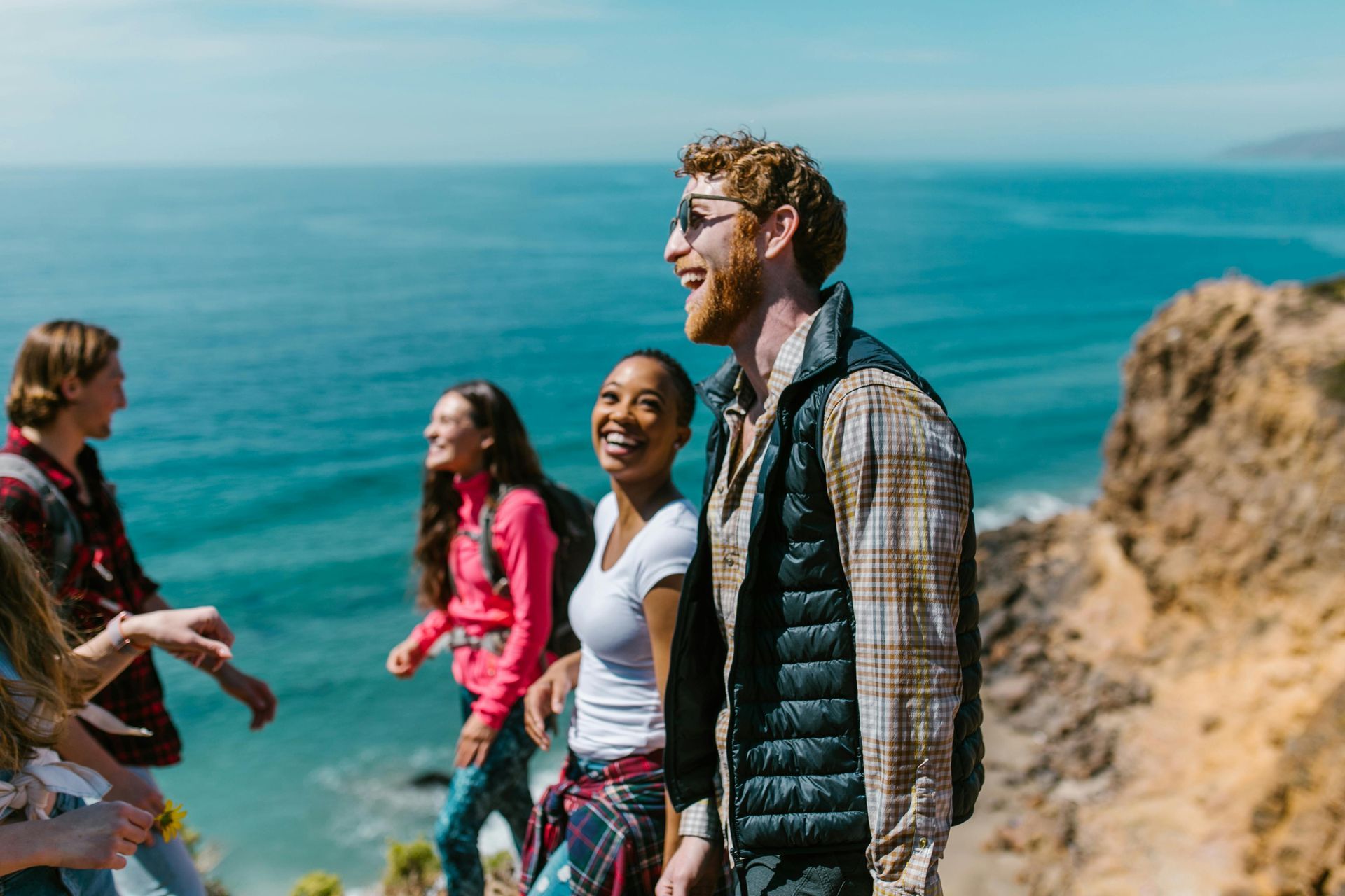A group of people are walking on a cliff overlooking the ocean.