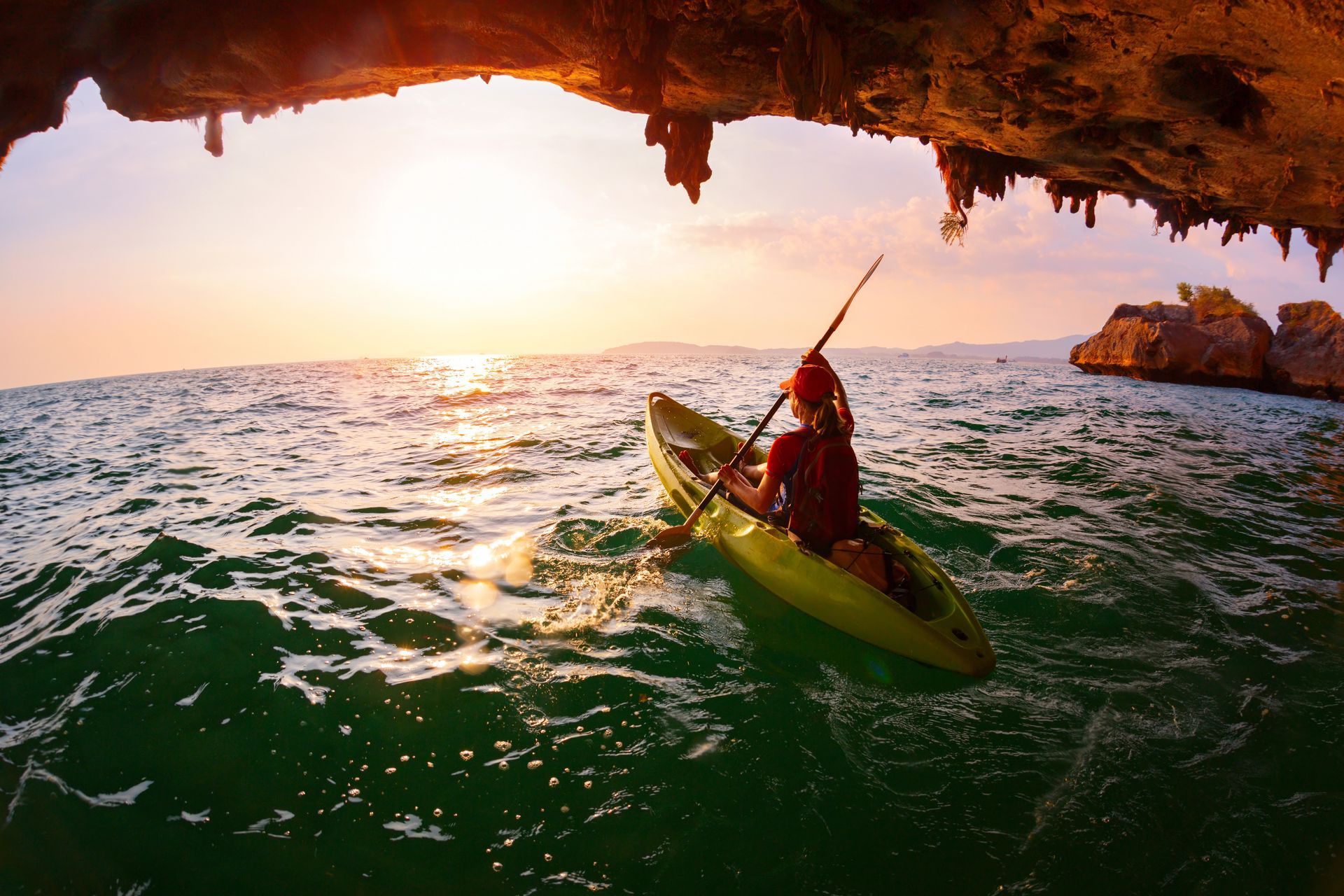 A person is paddling a kayak in the ocean under a cave.