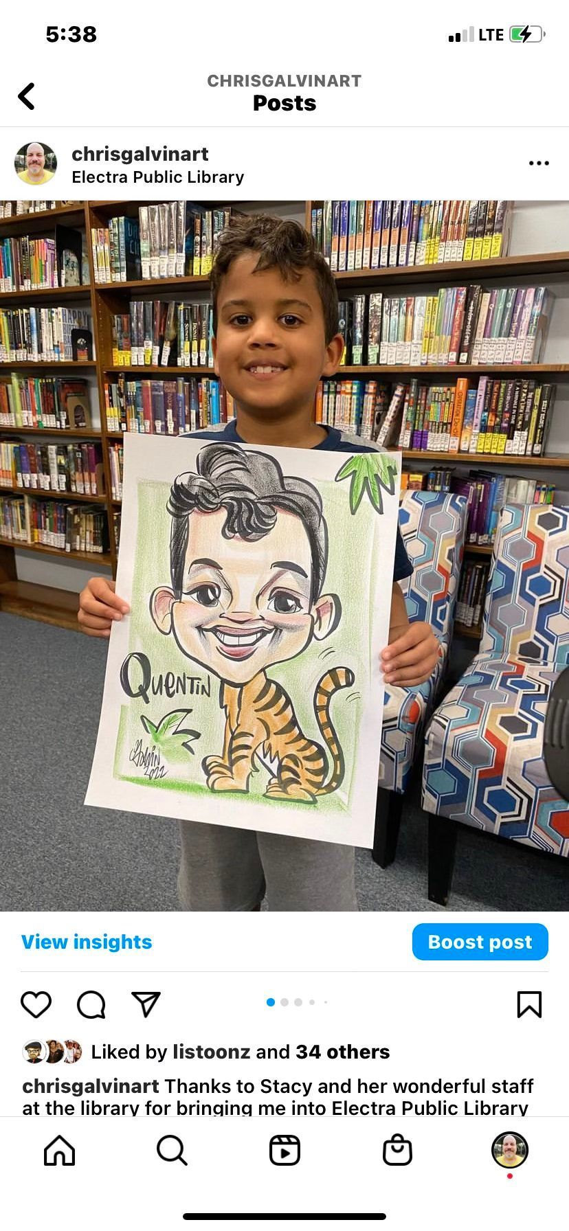 Boy in a bookstore holds a caricature drawing of himself, smiling with bookshelves behind him.