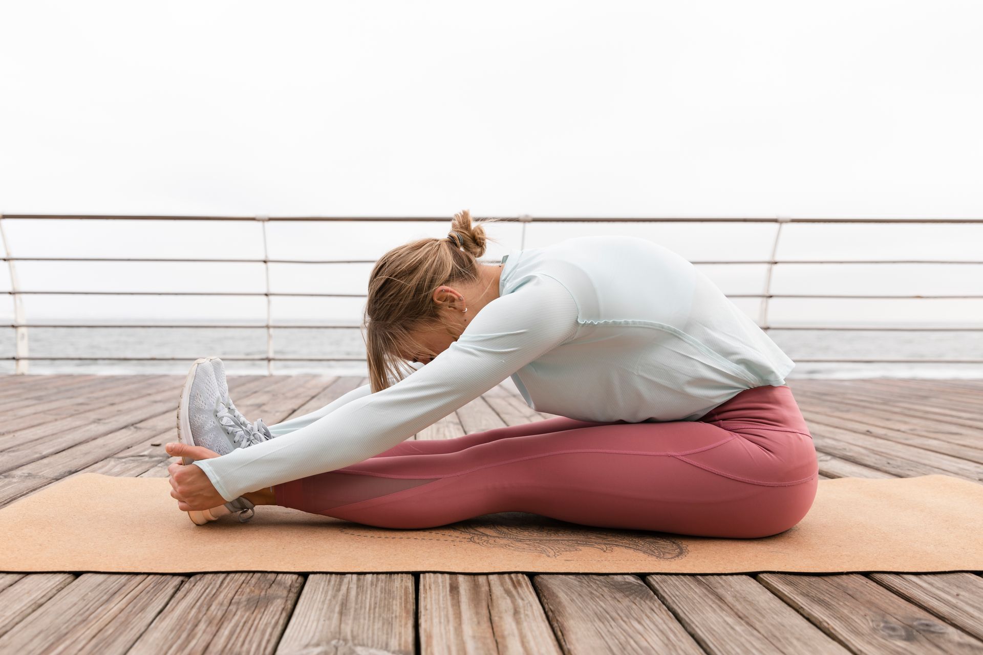 A woman is stretching her legs on a yoga mat on a wooden deck.