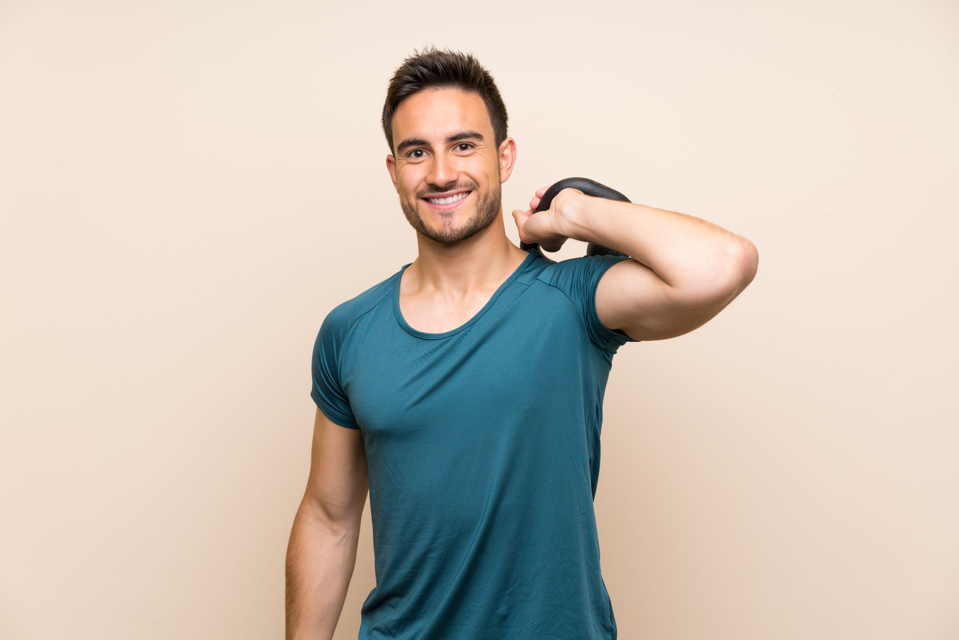 A young man is holding a kettlebell over his shoulder and smiling.