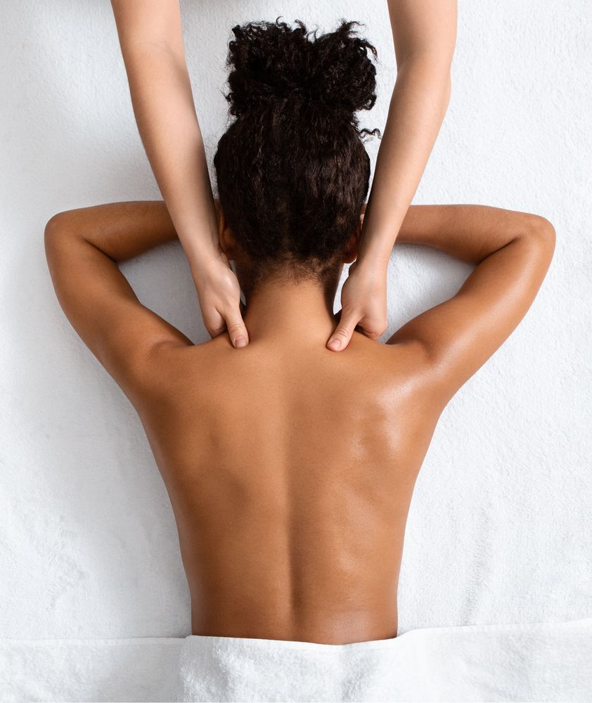 Person receiving a shoulder and neck massage on a white surface; hands of masseuse visible.