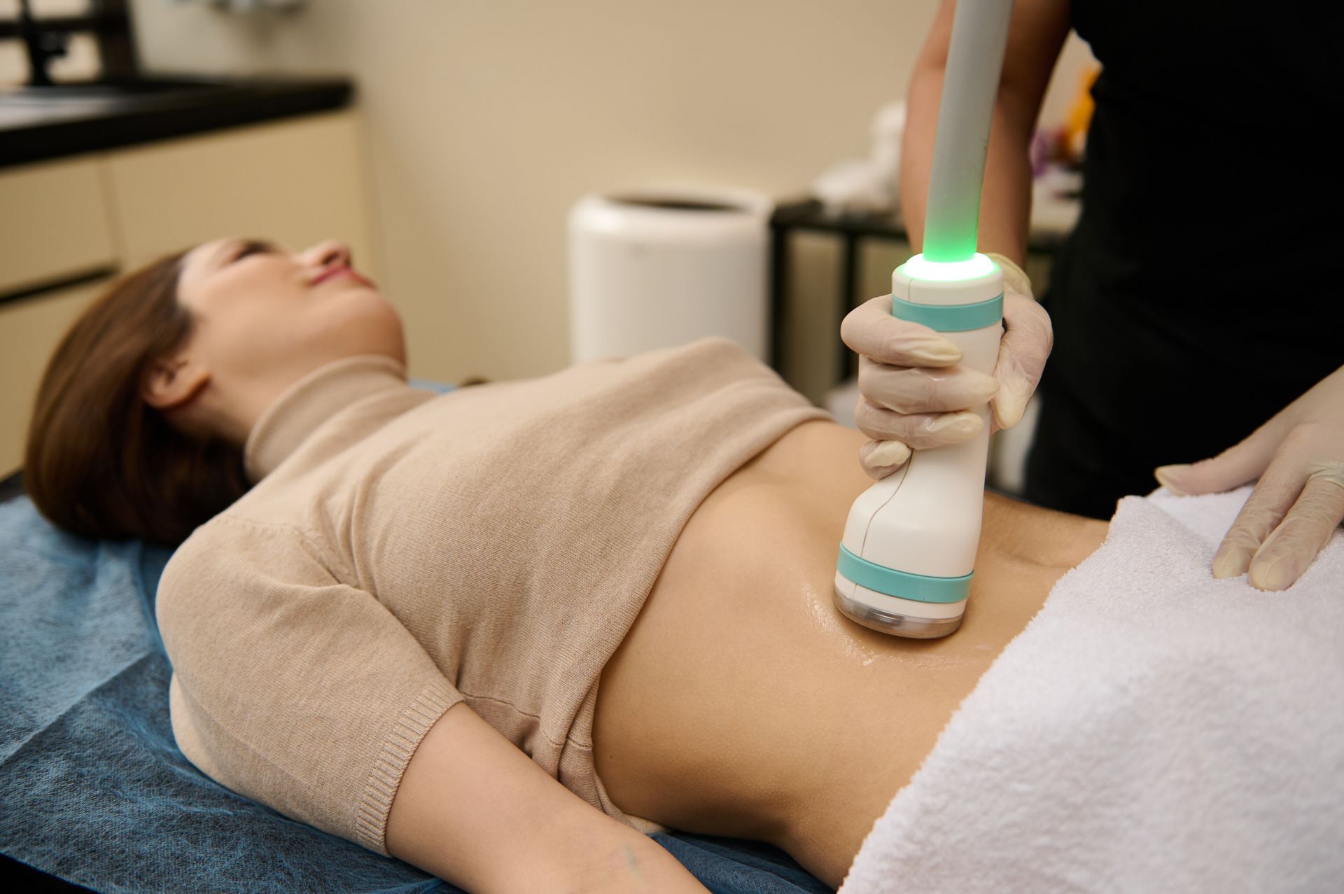 A woman is laying on a bed getting an ultrasound on her stomach.