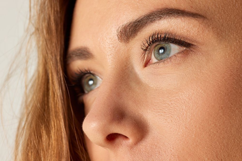 Close-up of a person's face with light blue eyes, prominent nose, and defined eyebrows, looking slightly to the side.