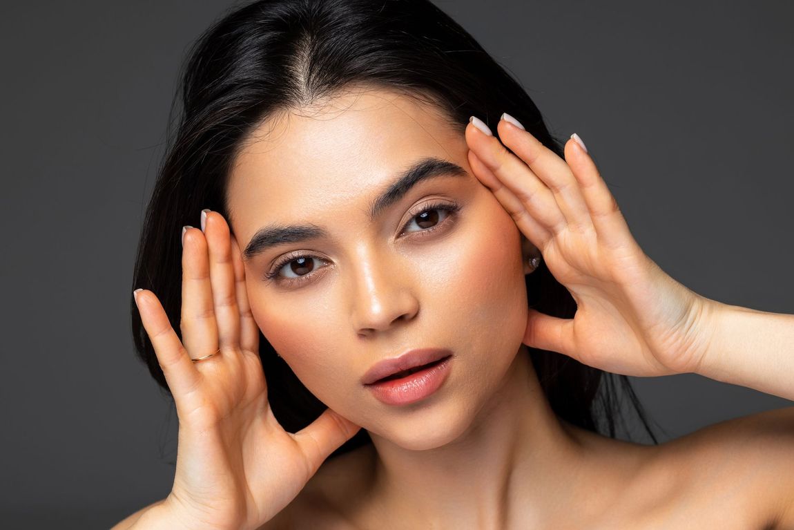 A woman with radiant skin has her palms on each side of her face