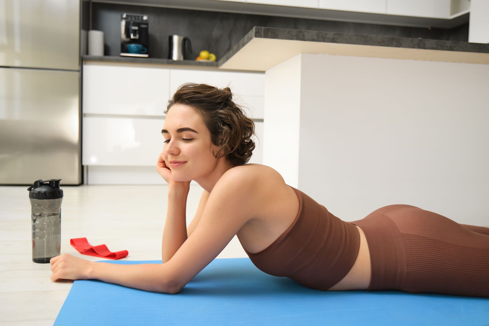 A woman is laying on a yoga mat in a kitchen.