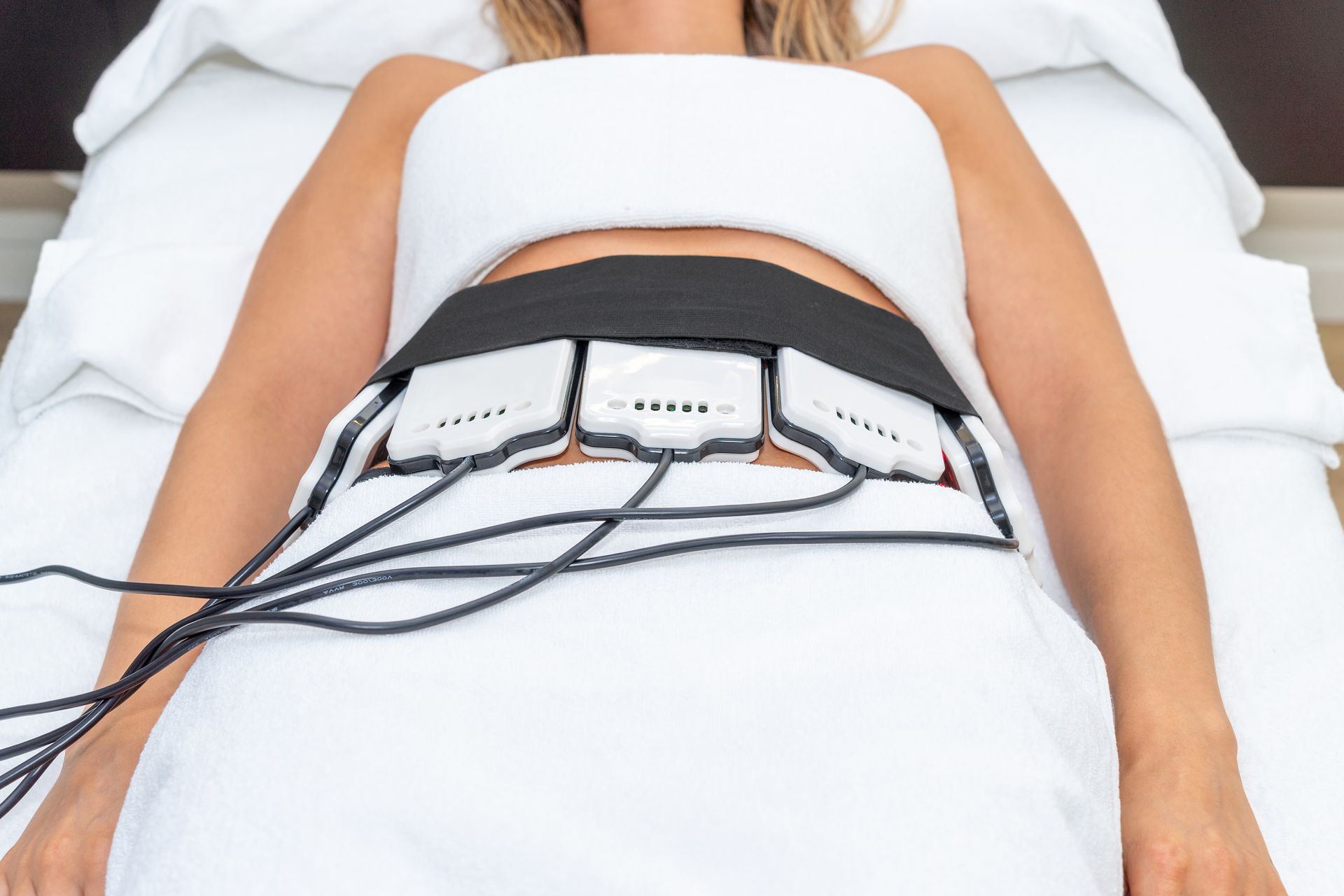 A woman is laying on a bed with a machine on her stomach.