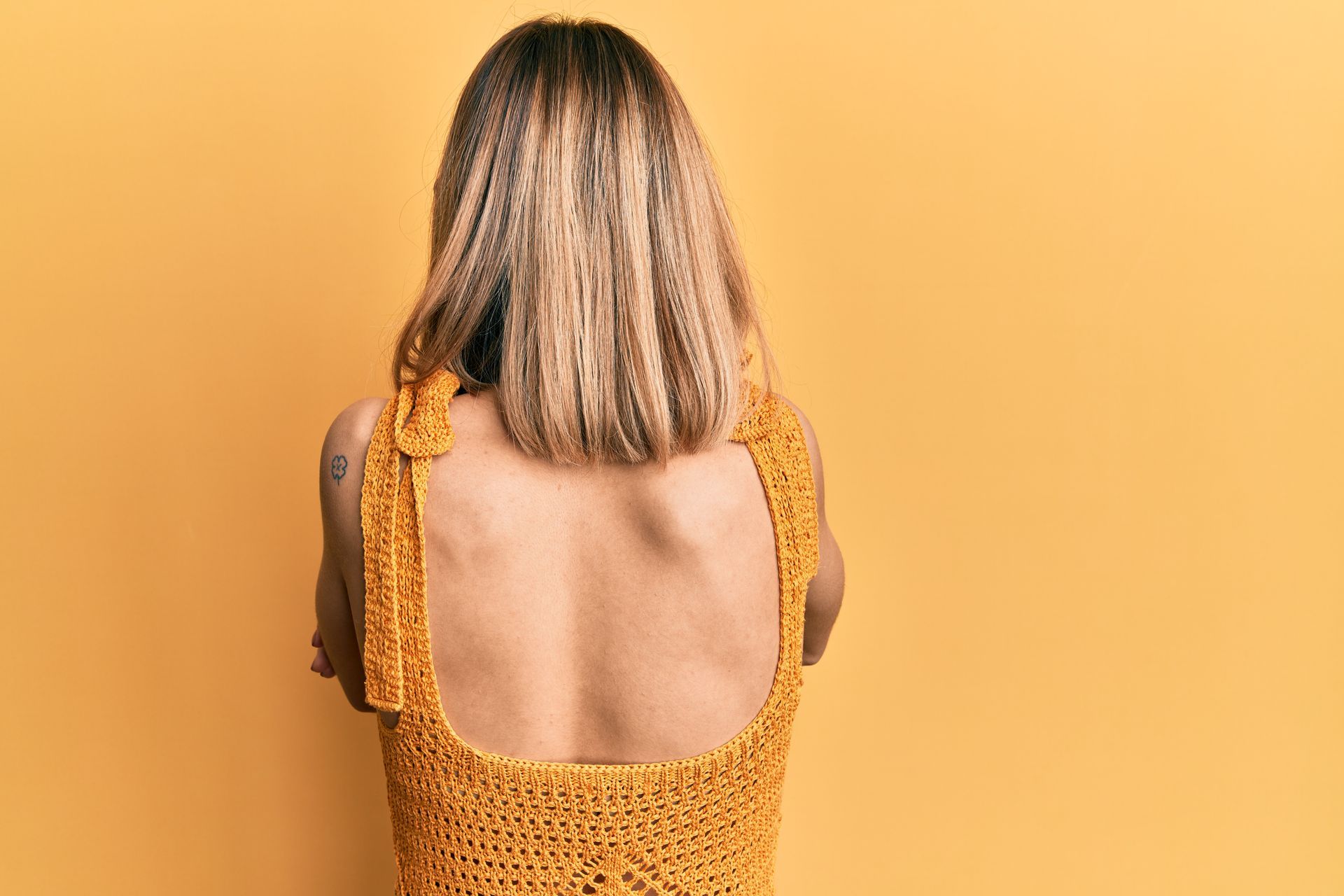 The back of a woman wearing a yellow swimsuit against a yellow background.