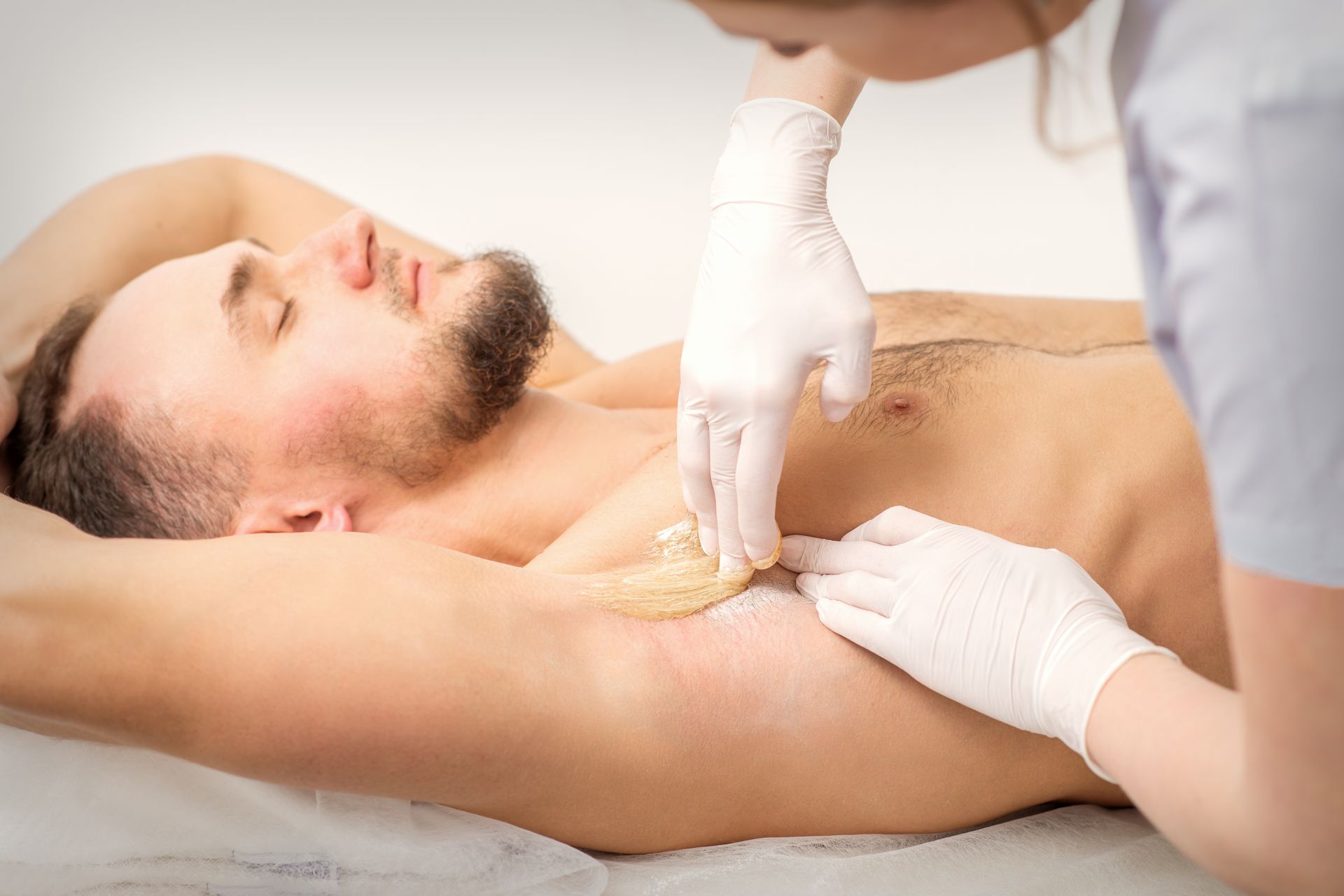 A man is getting his armpit waxed by a woman.