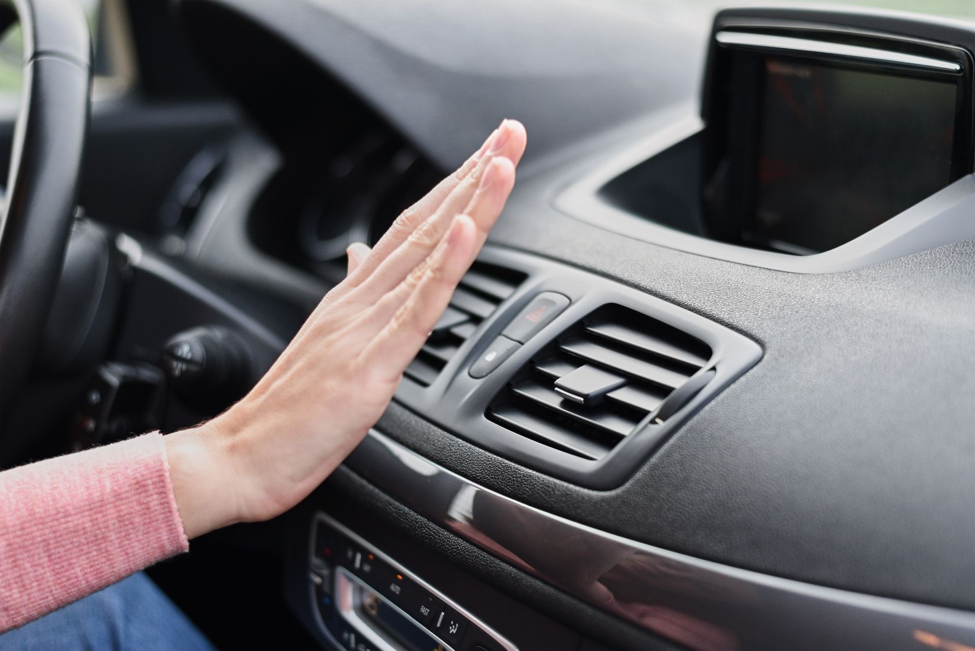 A woman is sitting in a car with her hand on the air vent.