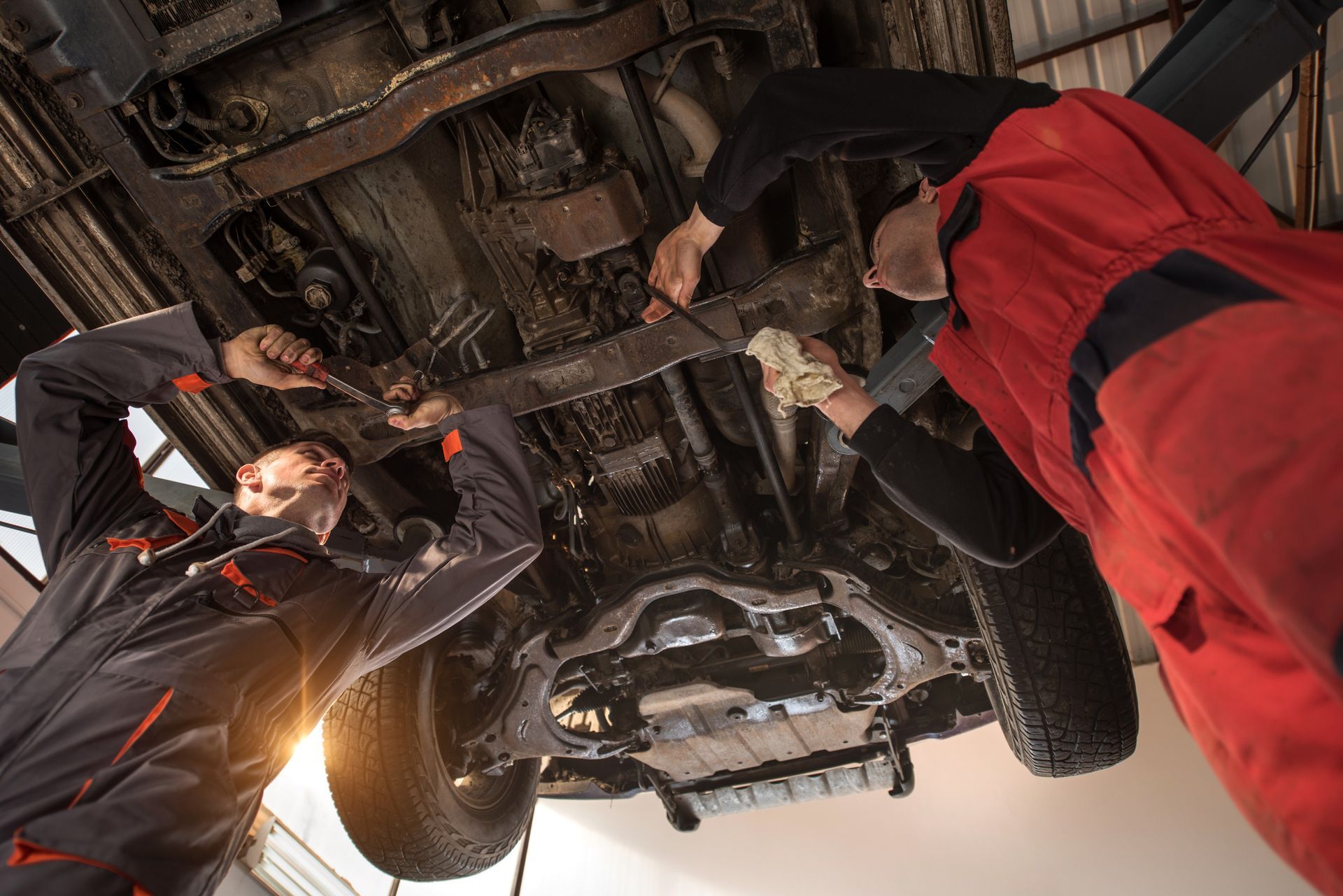 Two mechanics are working under a car in a garage.