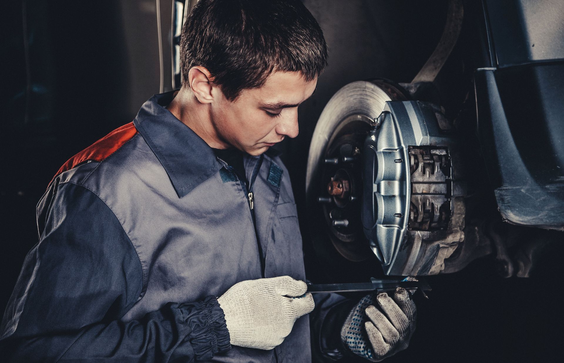 Professional car mechanic with dark hair, is performing brakes repair in auto service shop.