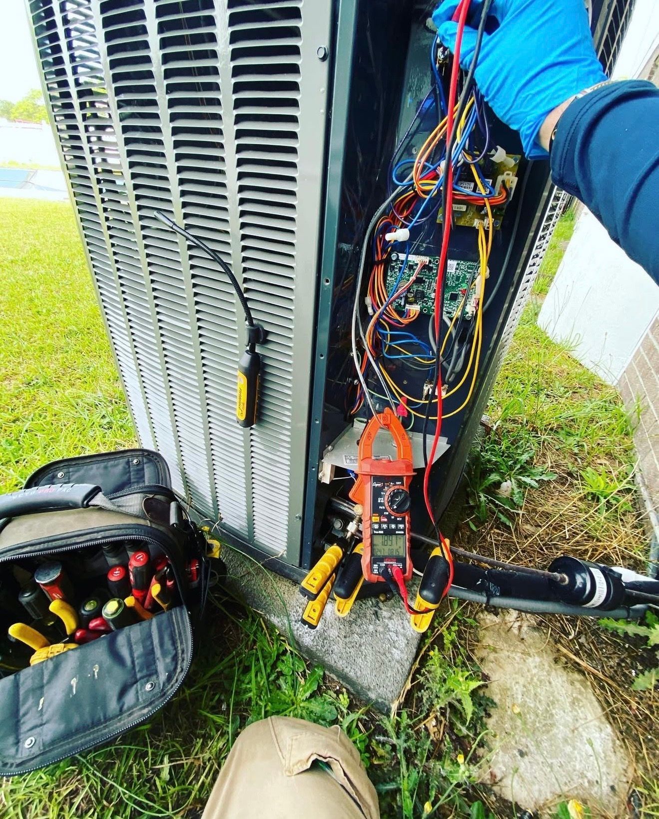 HVAC technician using multimeter on air conditioning unit, testing wires outdoors.