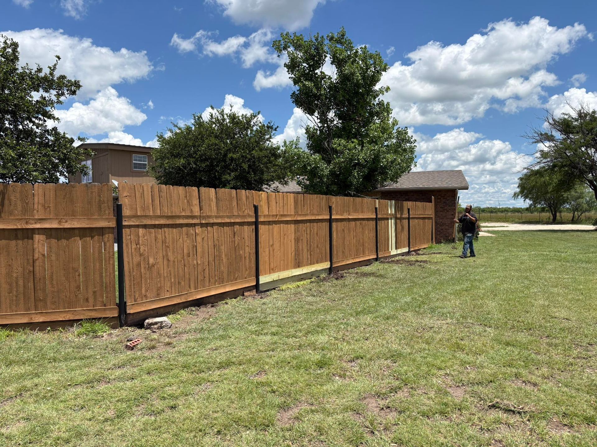 A man is standing in a grassy field next to a wooden fence.