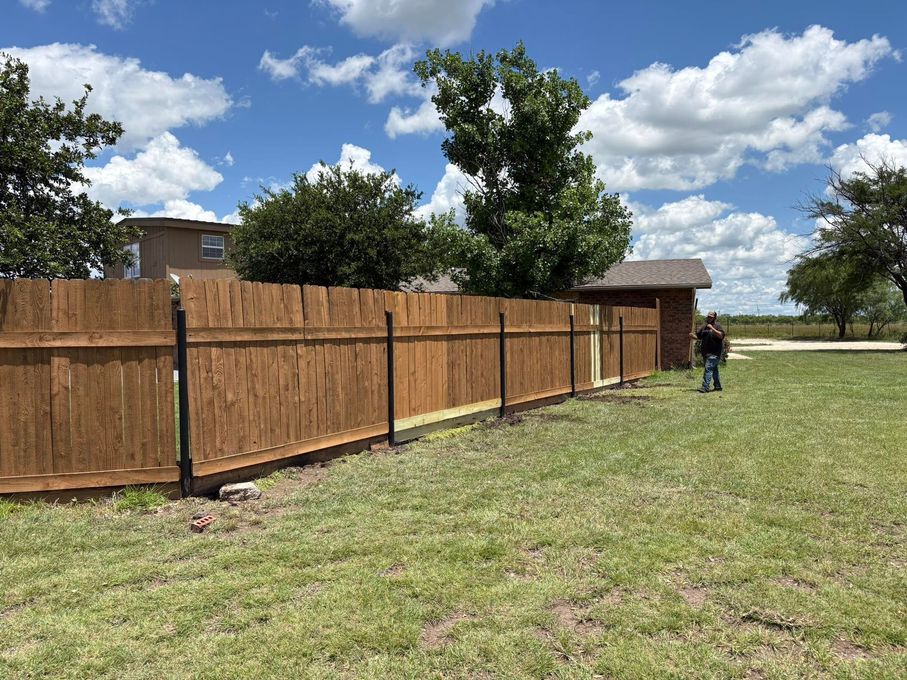 A wooden fence surrounds a swimming pool in a backyard.