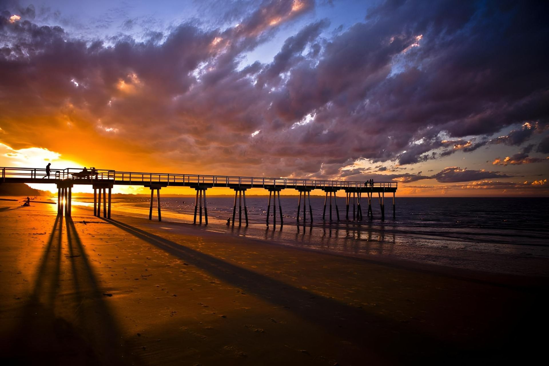 A Pier on a Beach at Sunset With People Standing on It — Active Tree Fellas in Hervey Bay, QLD