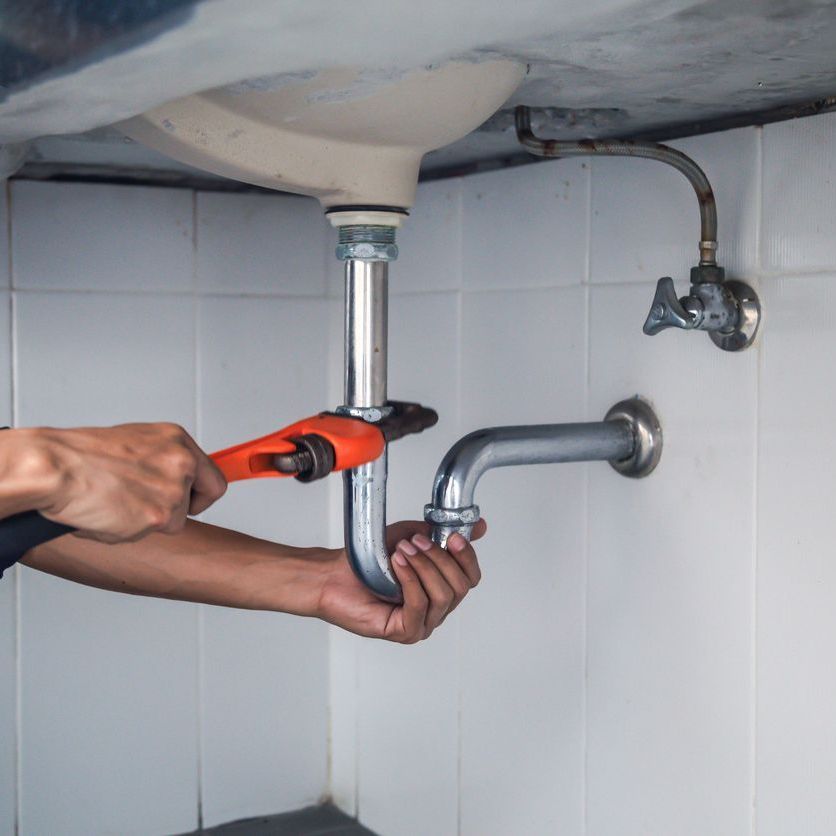 A man is fixing a sink pipe with a wrench