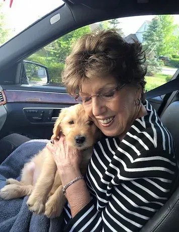 A woman is holding a puppy in her lap in a car.