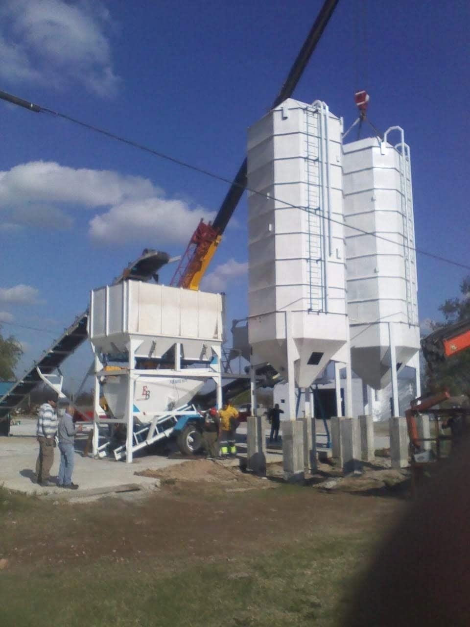 Una grúa está levantando un gran silo blanco en un campo.