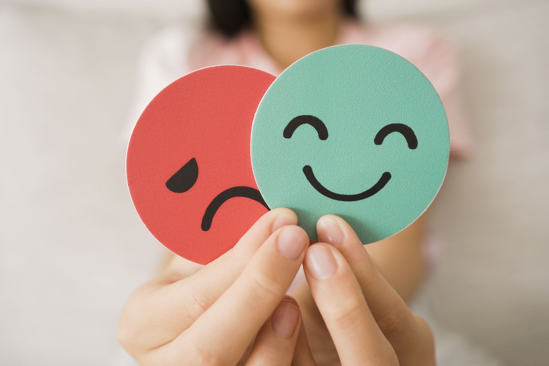 Hands holding two circular cards: one red with a sad face and one green with a happy face.