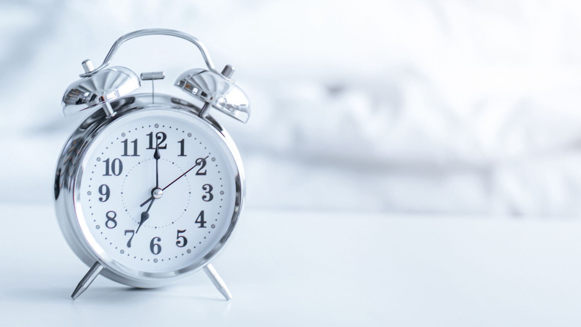 Silver alarm clock on a soft white background, showing approximately 7:30.