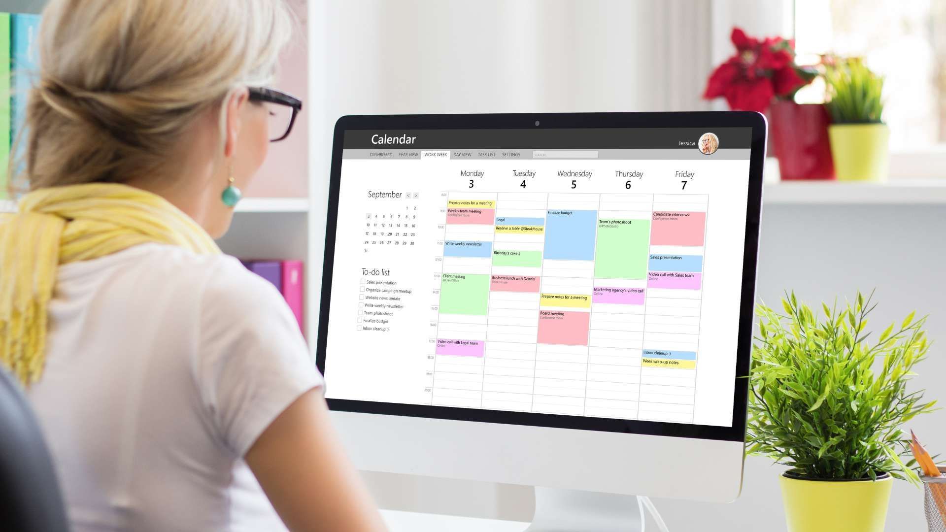 Person viewing a desktop calendar on a monitor in a bright office workspace