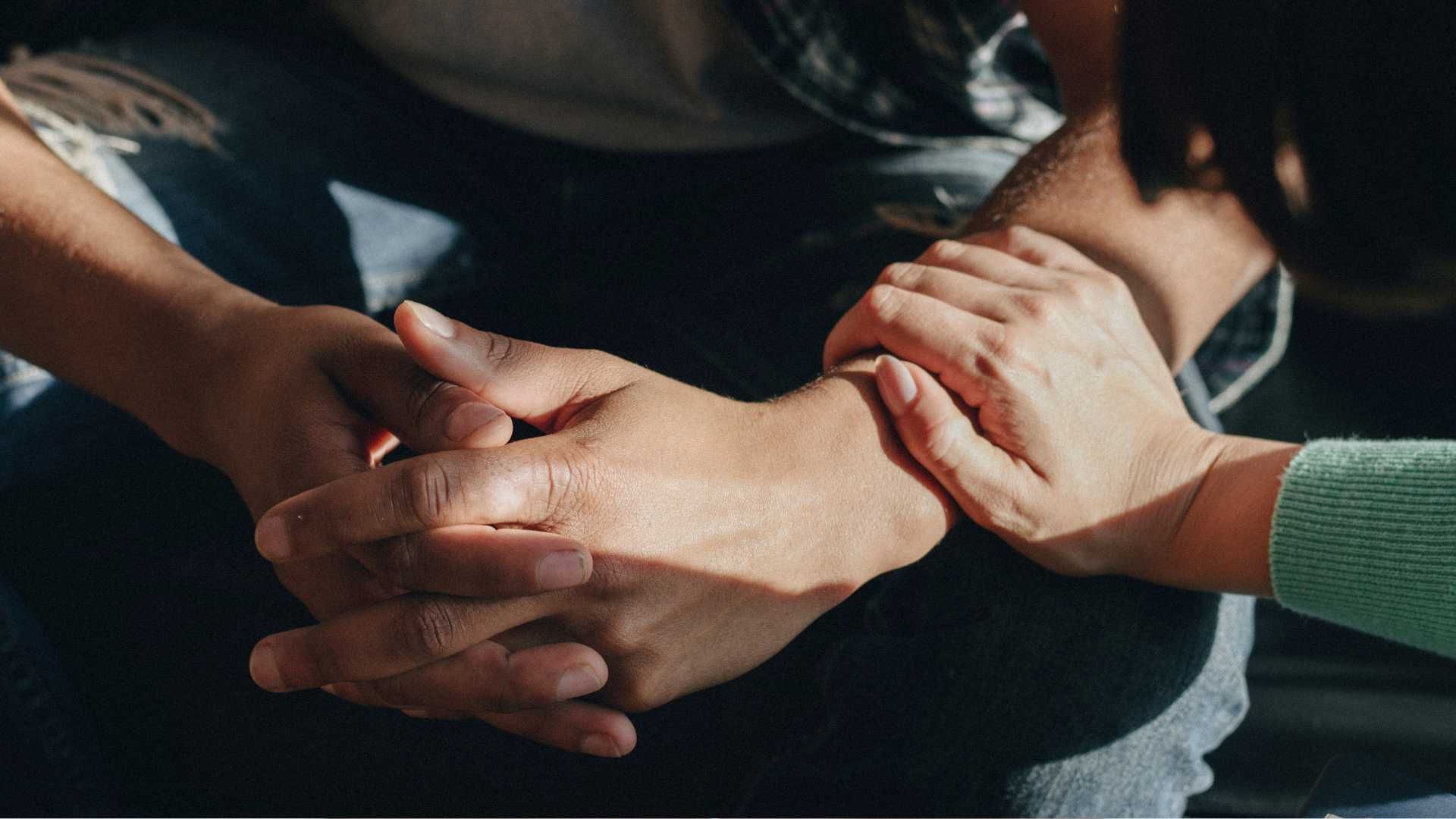 Two people clasping hands in a supportive gesture, one wearing a green sleeve.