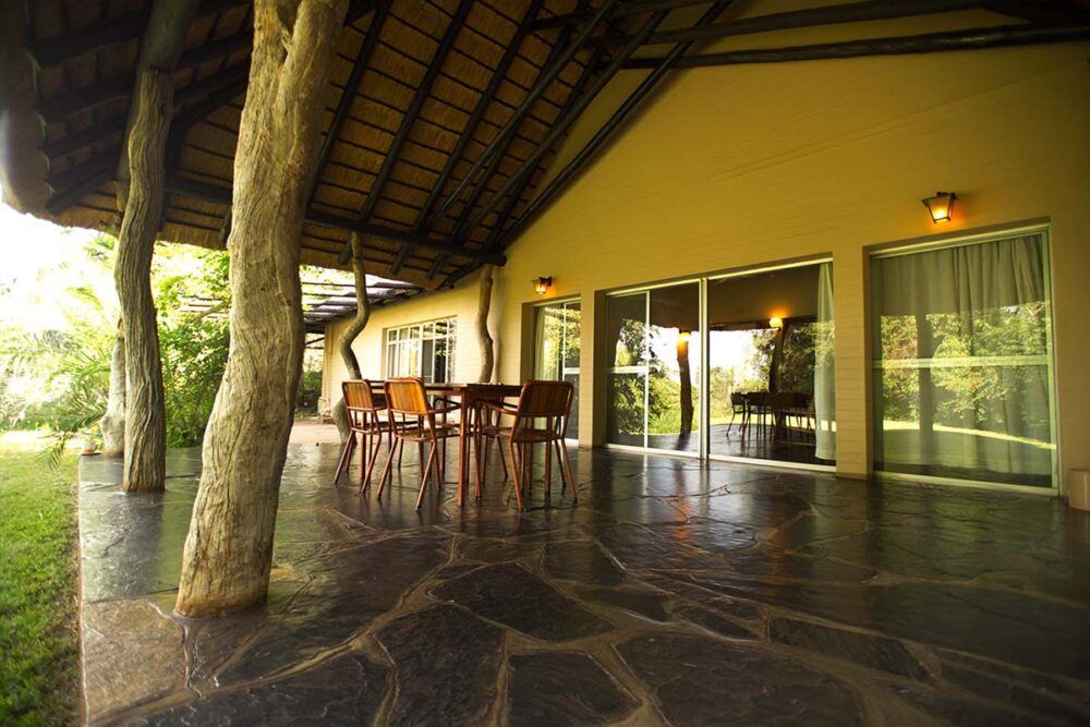 a patio with a table and chairs under a thatched roof at Satara Rest Camp in Kruger National Park