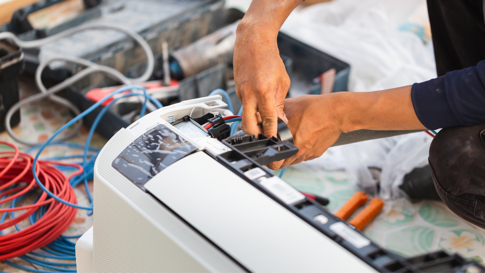 A man is fixing an air conditioner with a pair of pliers.