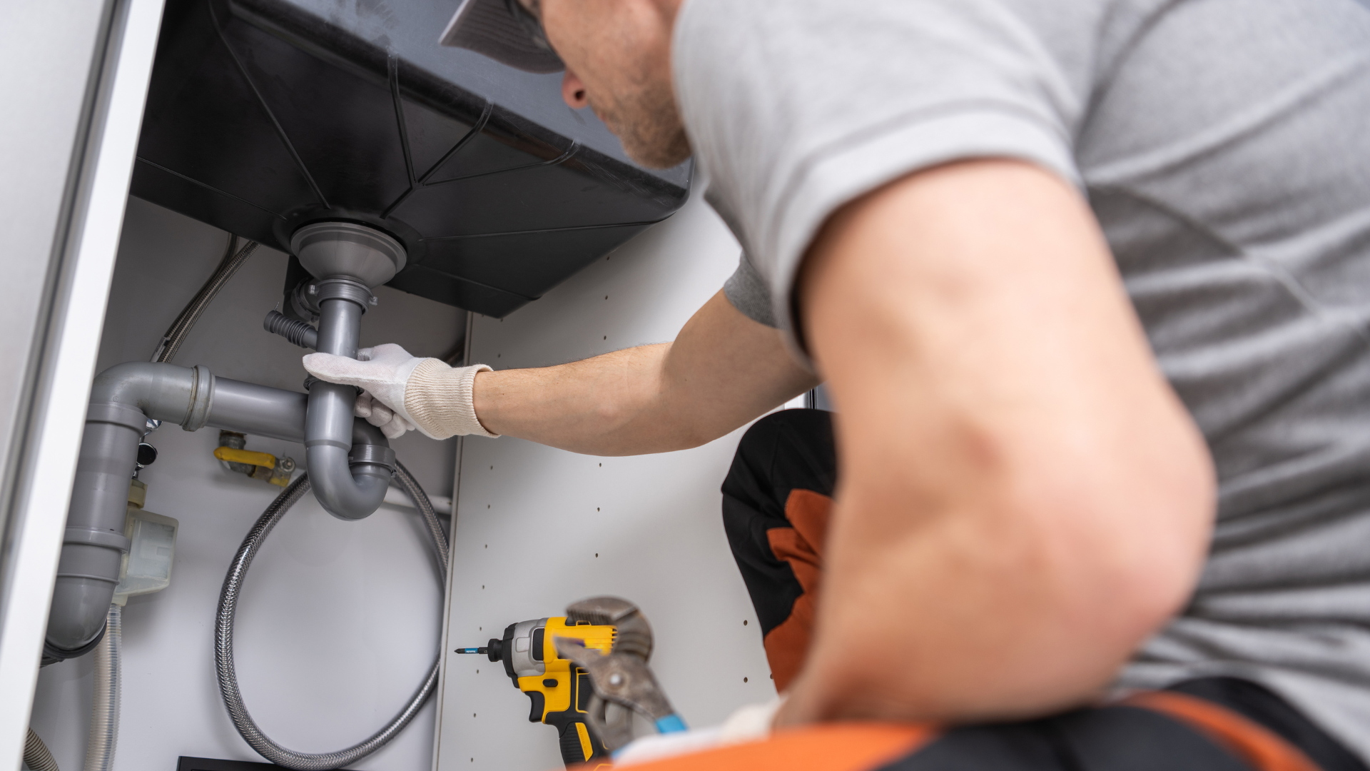 A plumber is fixing a sink in a kitchen with a drill.