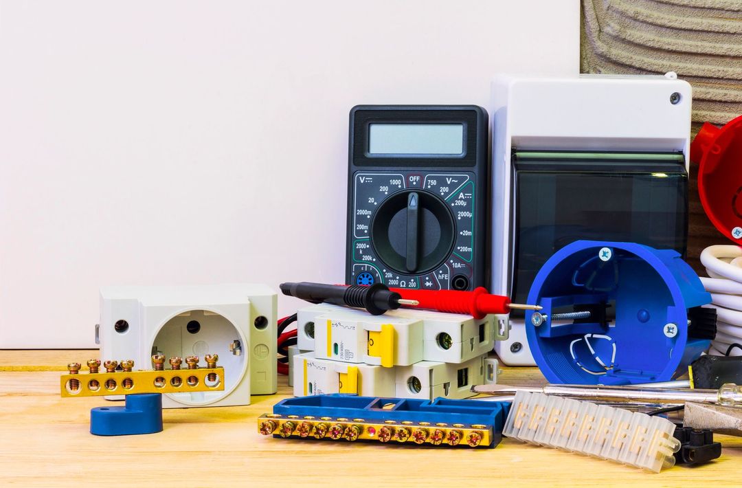 Utensili e componenti elettrici su una superficie di legno, tra cui un multimetro e degli interruttori automatici.