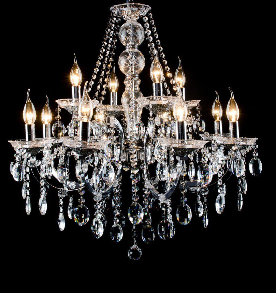 Lampadario di cristallo con lampadine accese a forma di candela appese su uno sfondo nero.