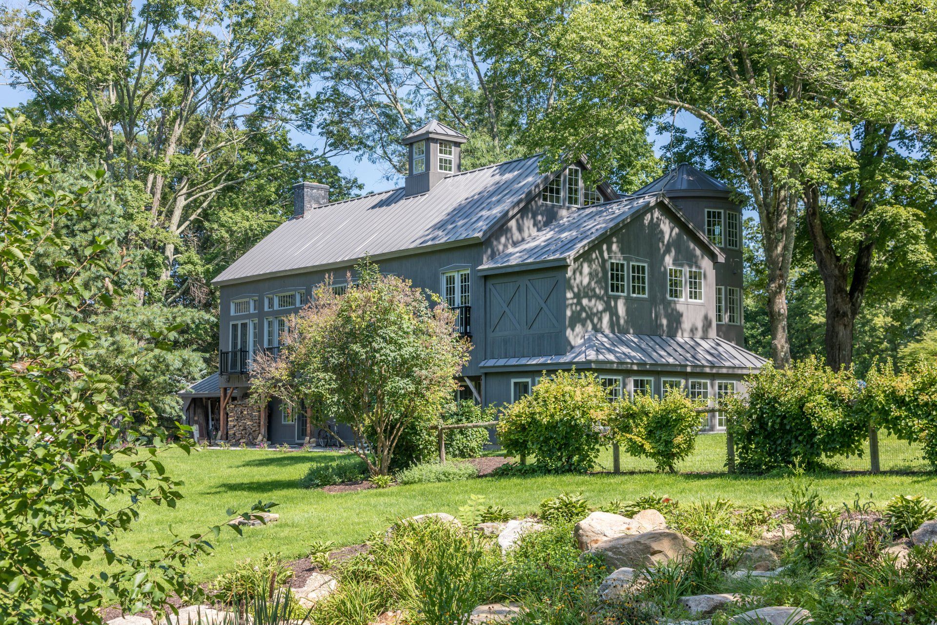 A large house is sitting in the middle of a lush green field surrounded by trees.