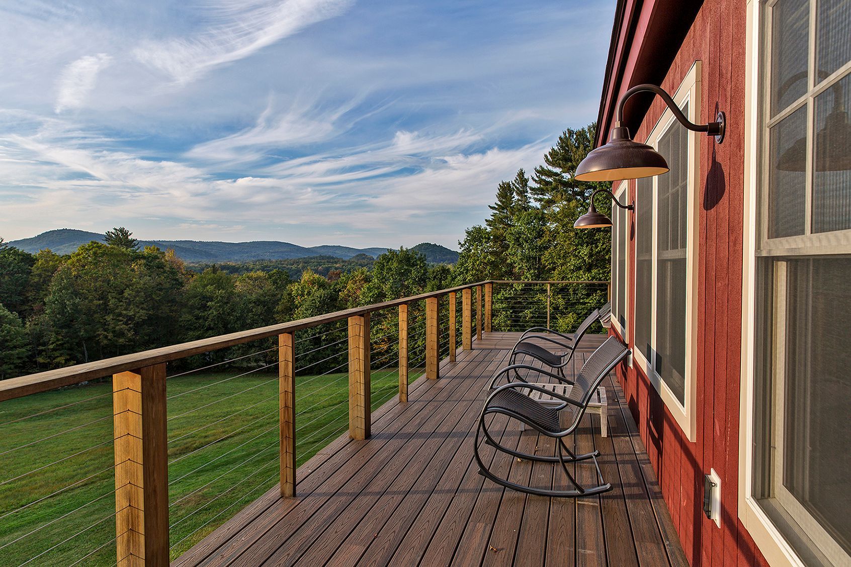 A red barn with a wooden deck and rocking chairs on it.
