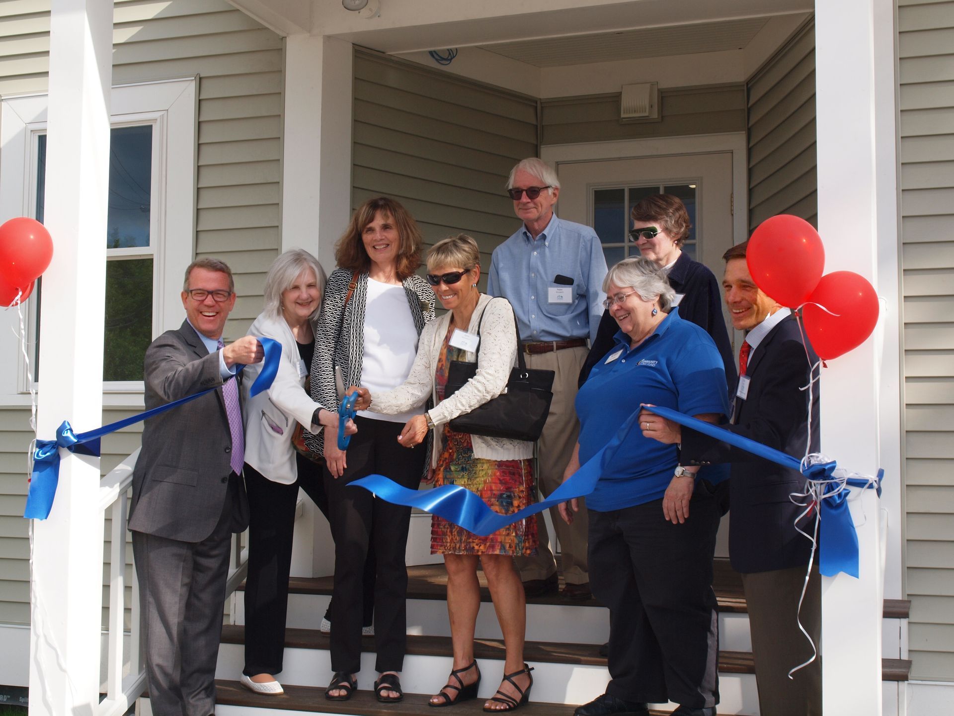A group of people are cutting a blue ribbon in front of a house