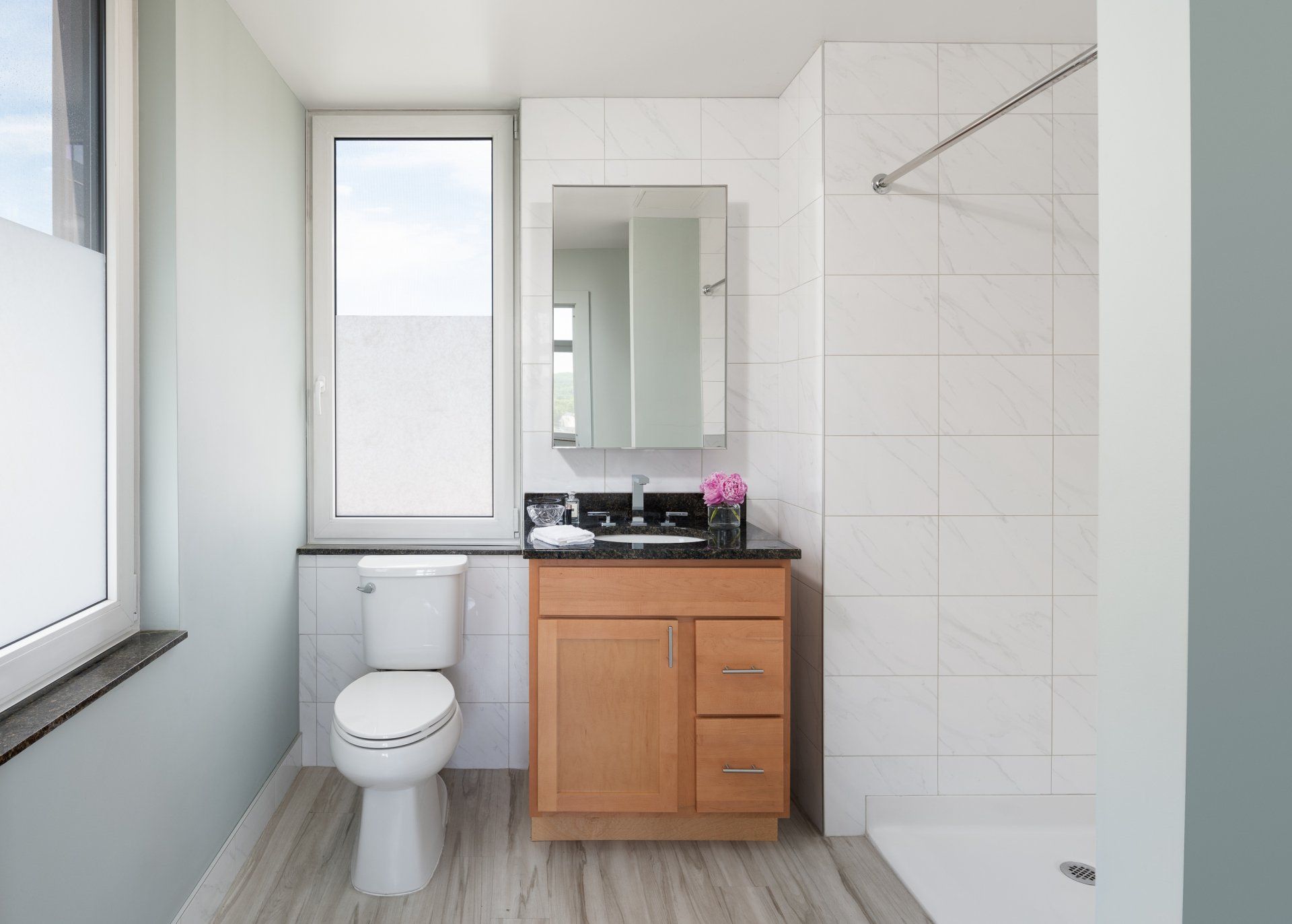 A bathroom with a toilet , sink , mirror and shower.