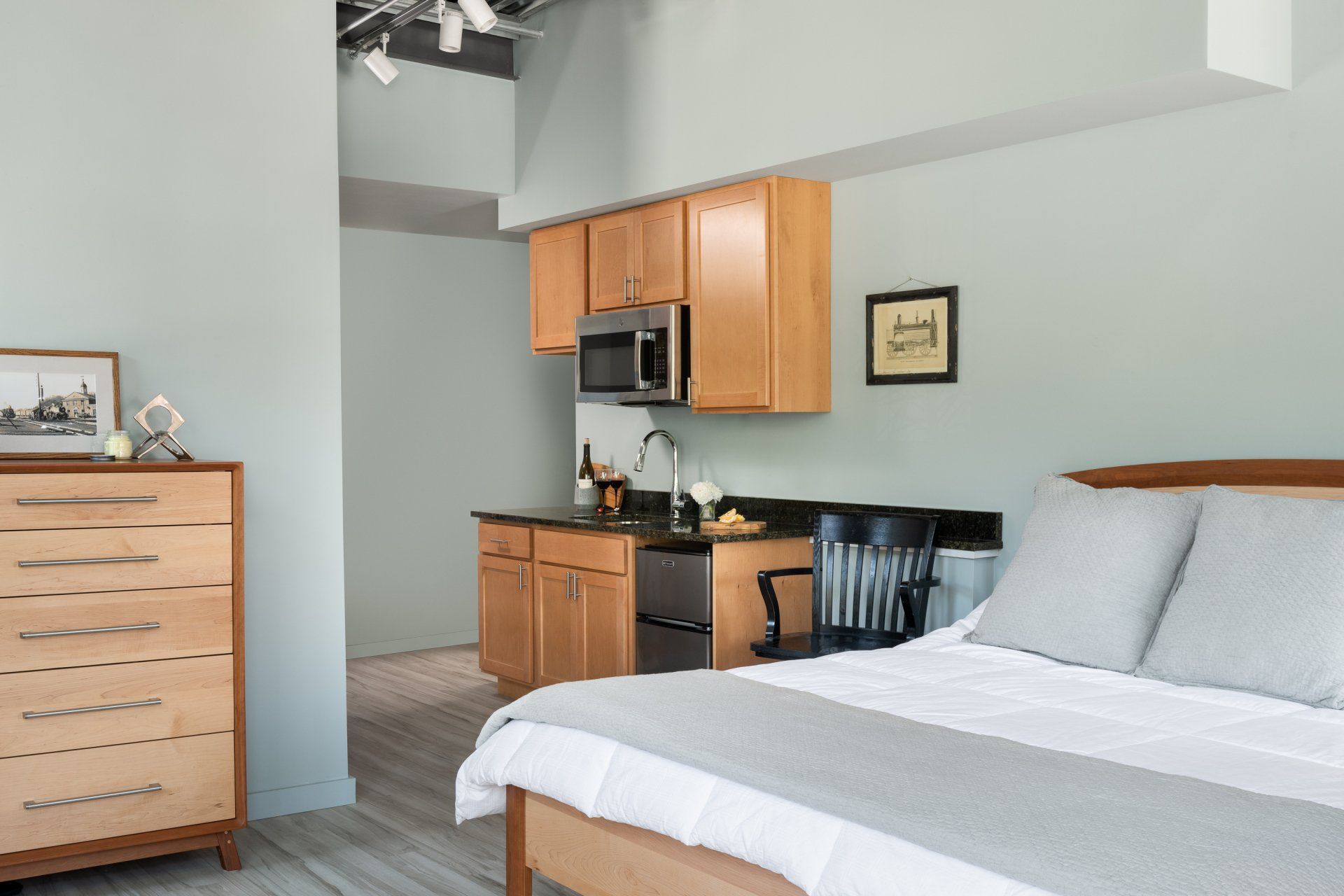 A bedroom with a bed , dresser , chair and kitchen.