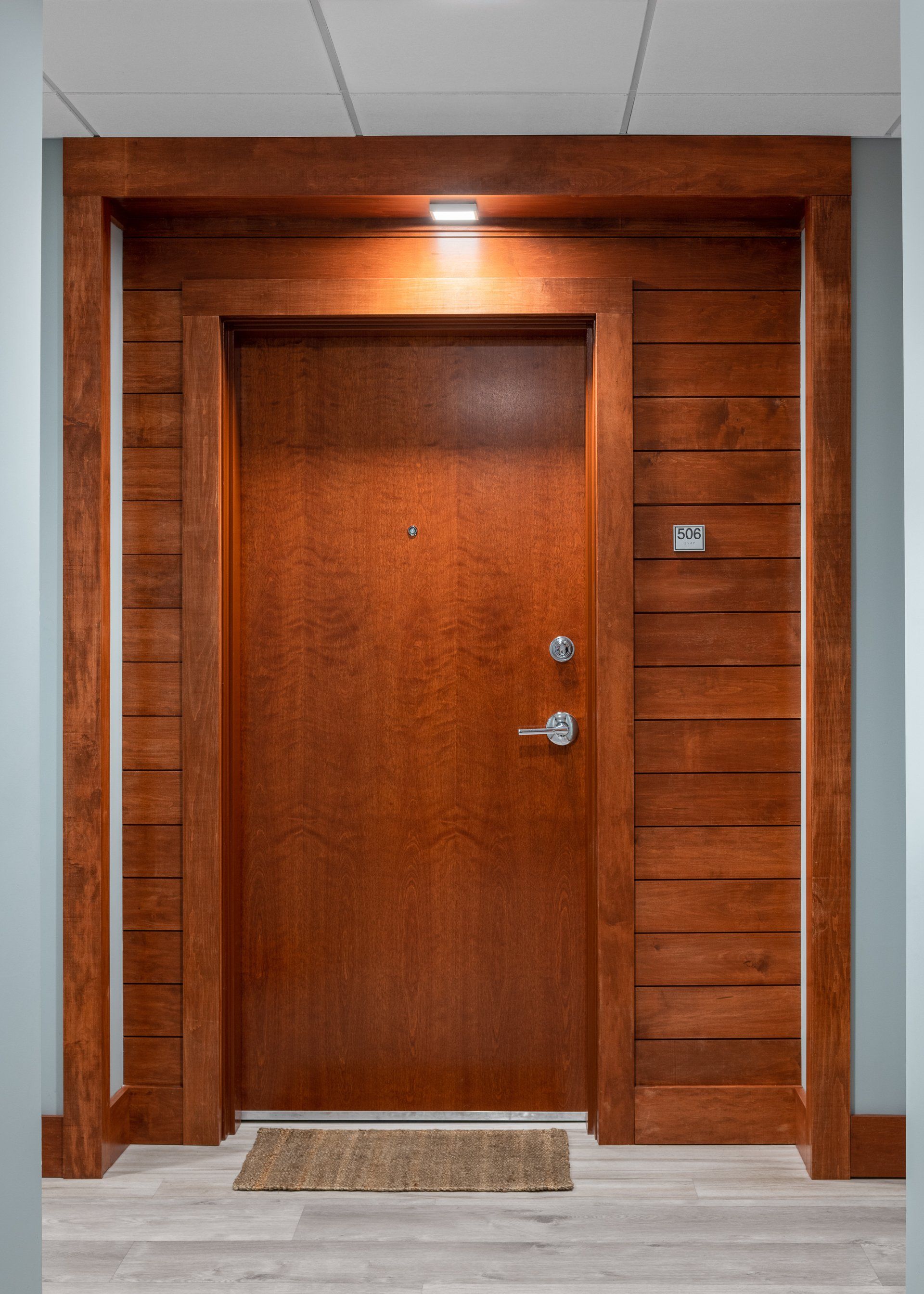 A wooden door with a rug on the floor in a hallway.