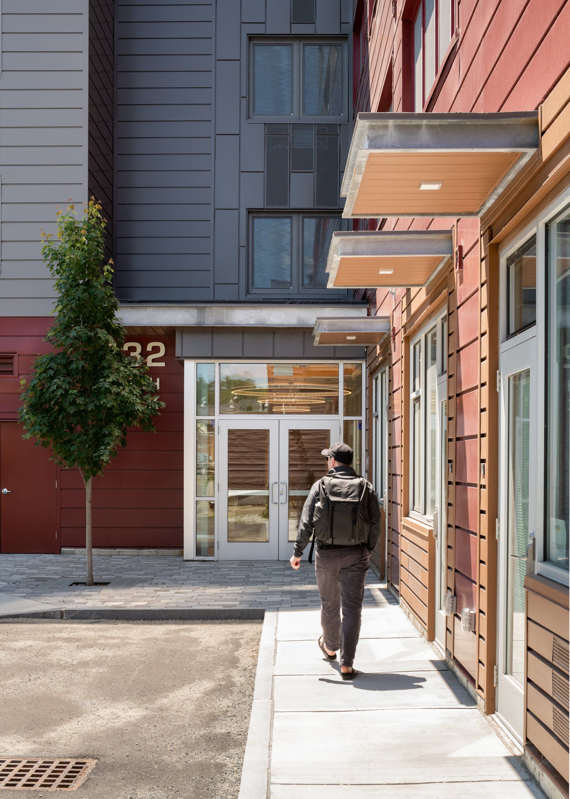 A man is walking down a sidewalk in front of a building with the number 32 on it.