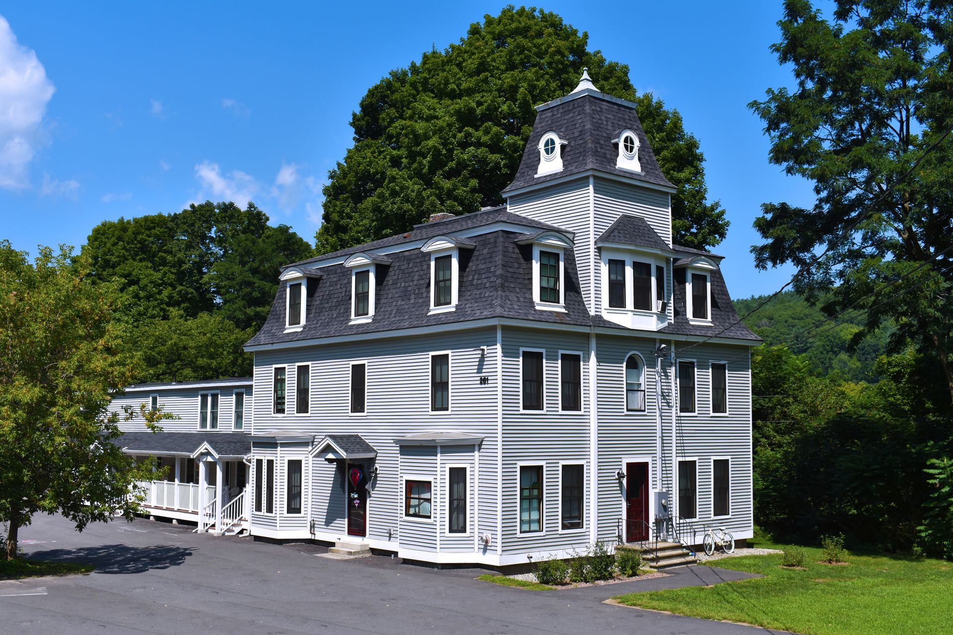 A large white house with a black roof is surrounded by trees and grass.