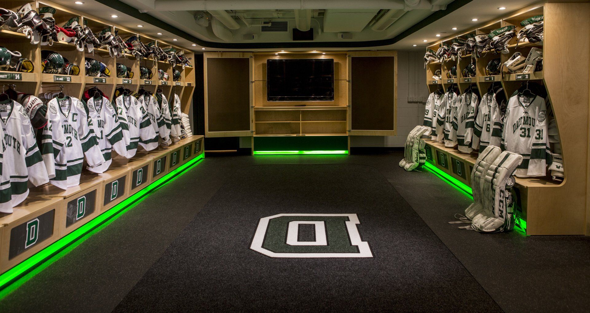 A hockey locker room with lots of jerseys and green lights.